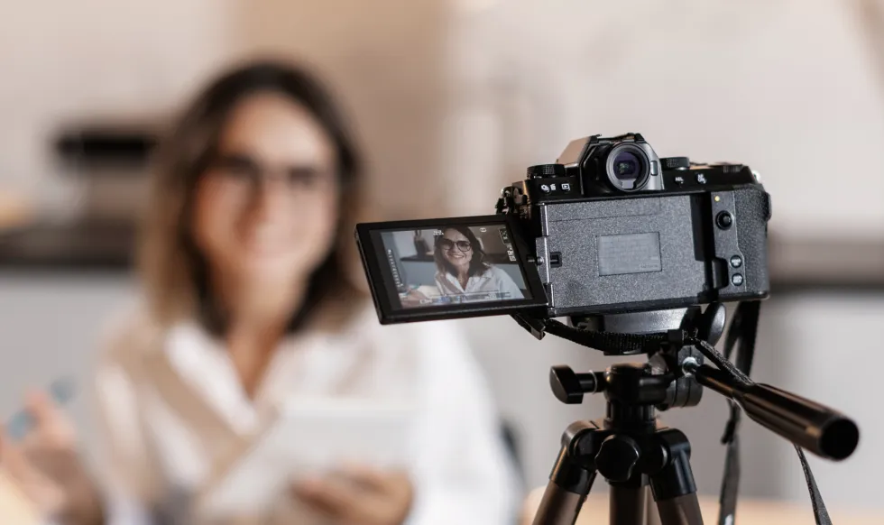 A camera on a tripod stand recording a lady sitting