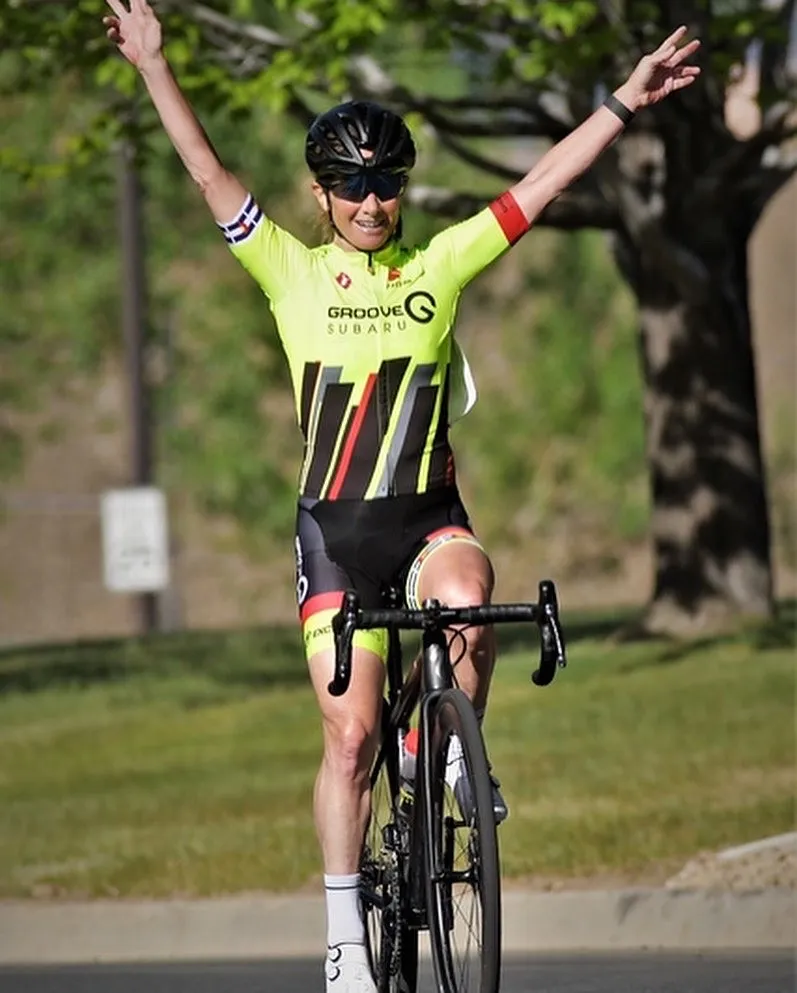 A woman on a bicycle stretching her hands up wide while cycling.