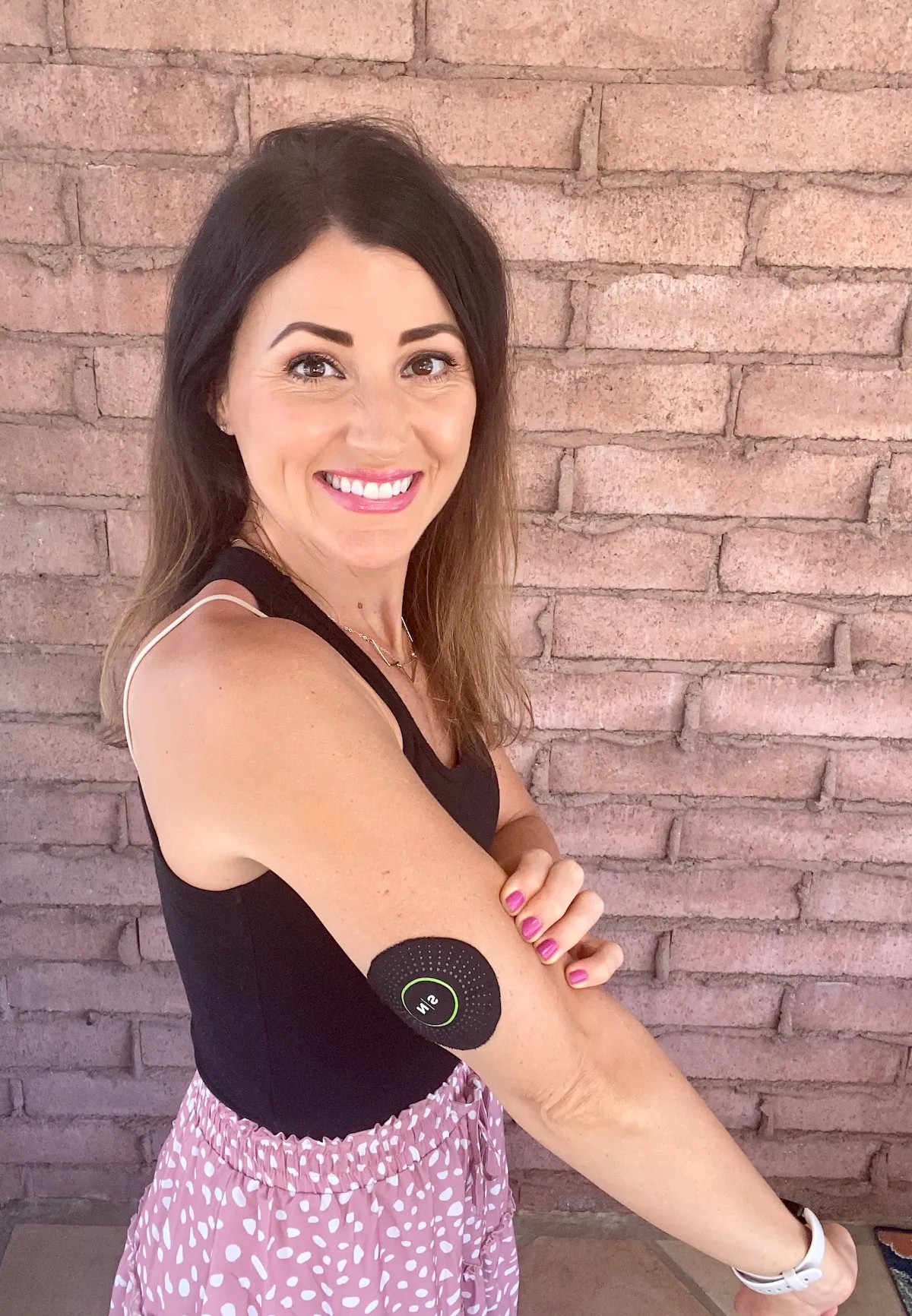 A happy Nutrisense member standing on her right side view with a Nutrisense cgm sensor on her upper right hand.