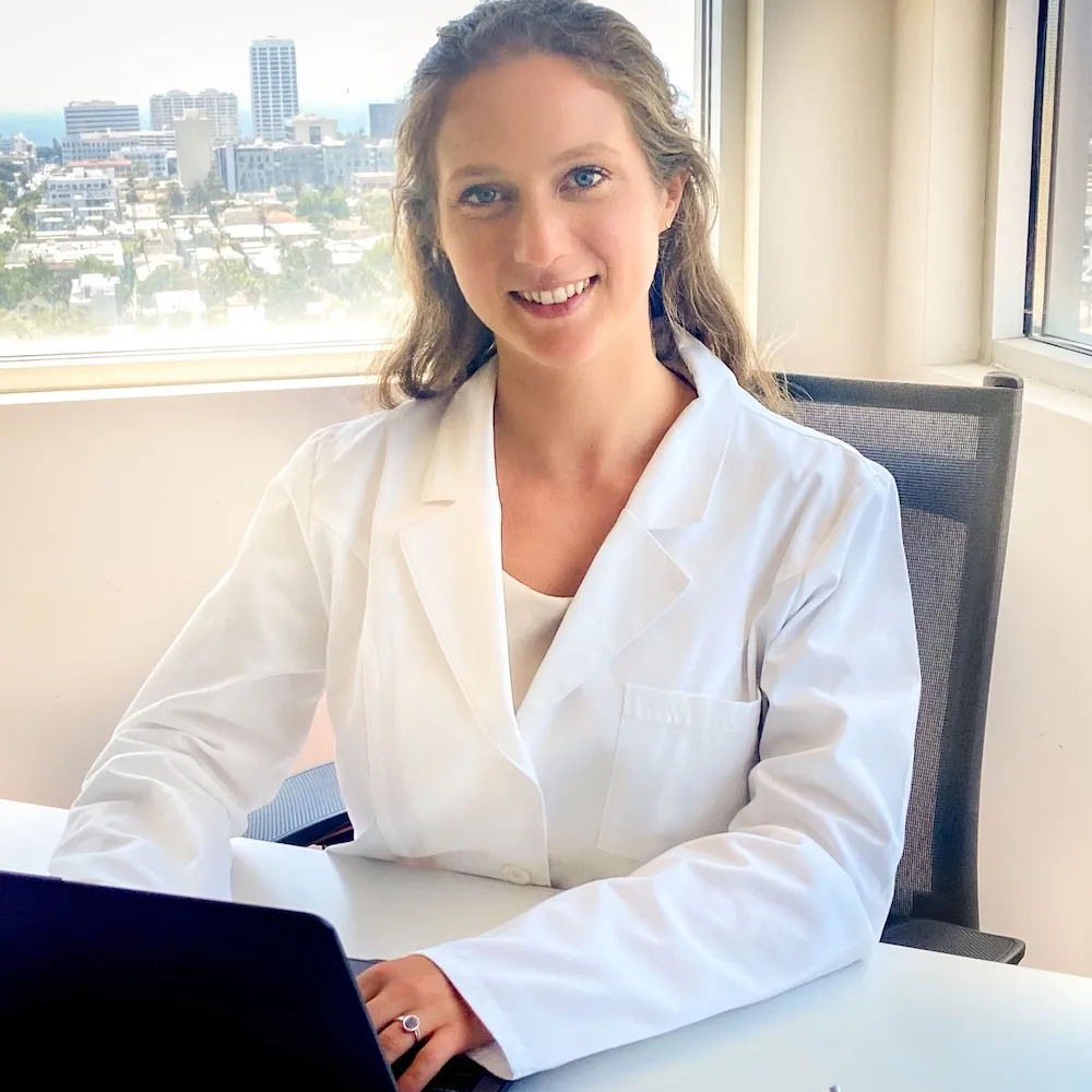 A Nutrisense member Katie Reines siting with both of her hands on her laptop with smiley face.