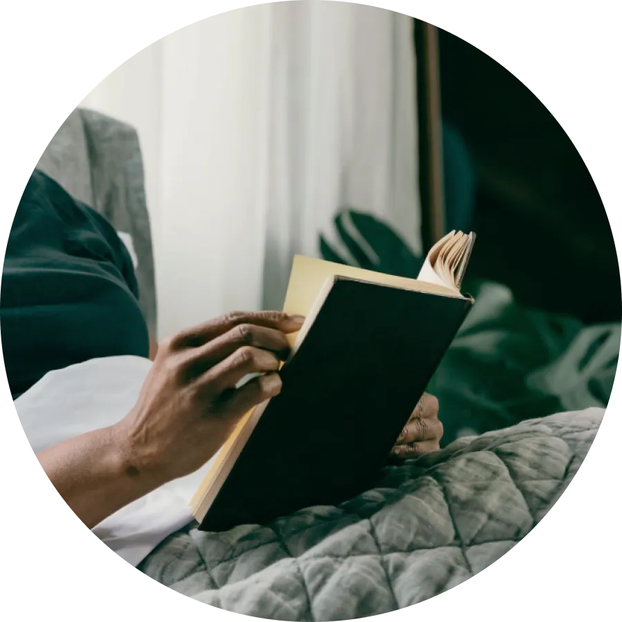 A book held by female hands who seems to be laying on bed.