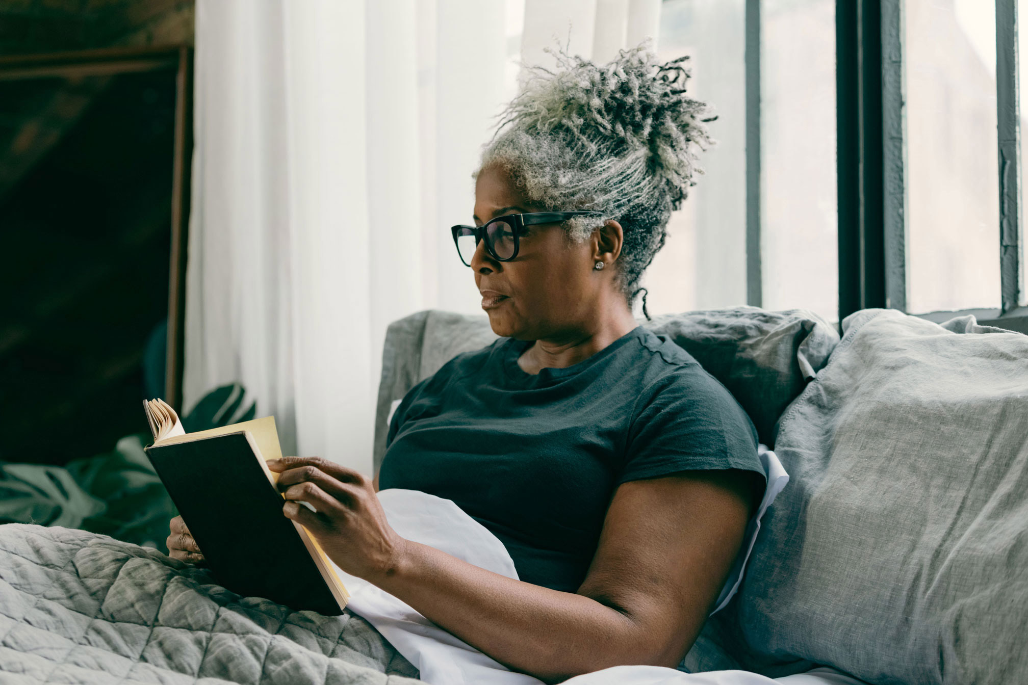 A Nutrisense member reading a book on bed while wearing a CGM sensor on her left upper hand