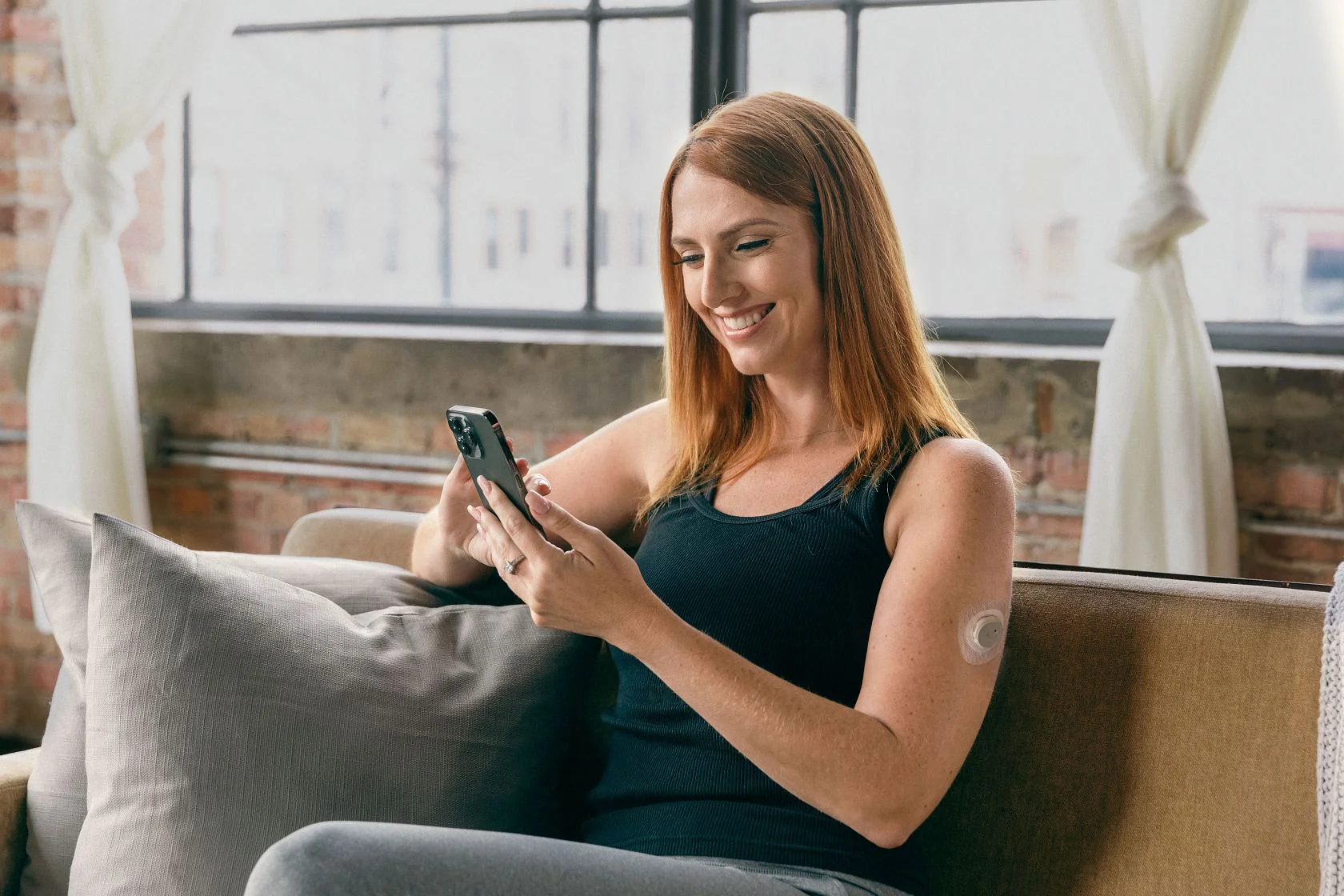 A Nutrisense member smiling while looking at her phone while wearing a CGM sensor on her left upper hand
