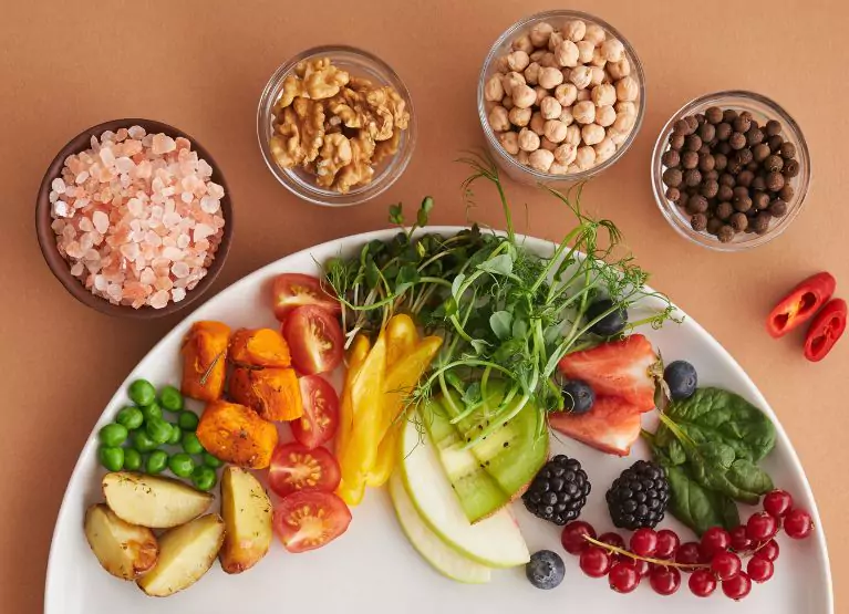 A table of whole foods including walnuts, peppers, chickpeas, berries, Himalayan salt, apples, greens, tomatoes, potatoes, and peas