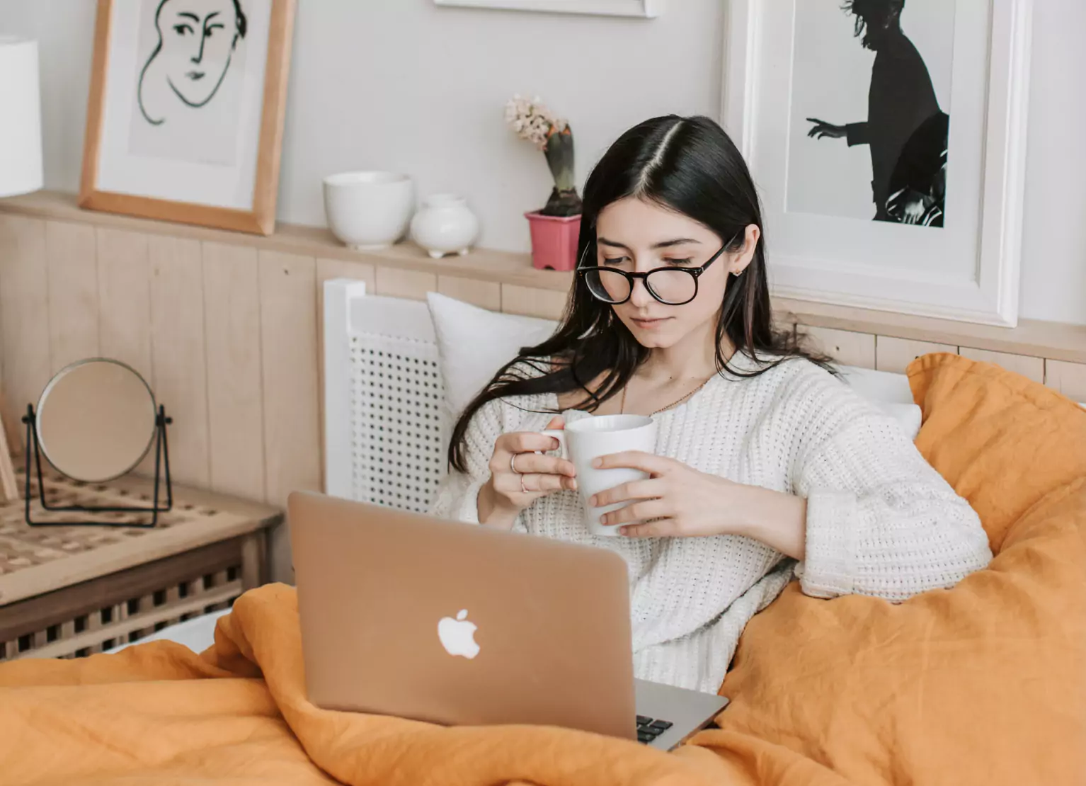 a person curled up on bed and looking at laptop