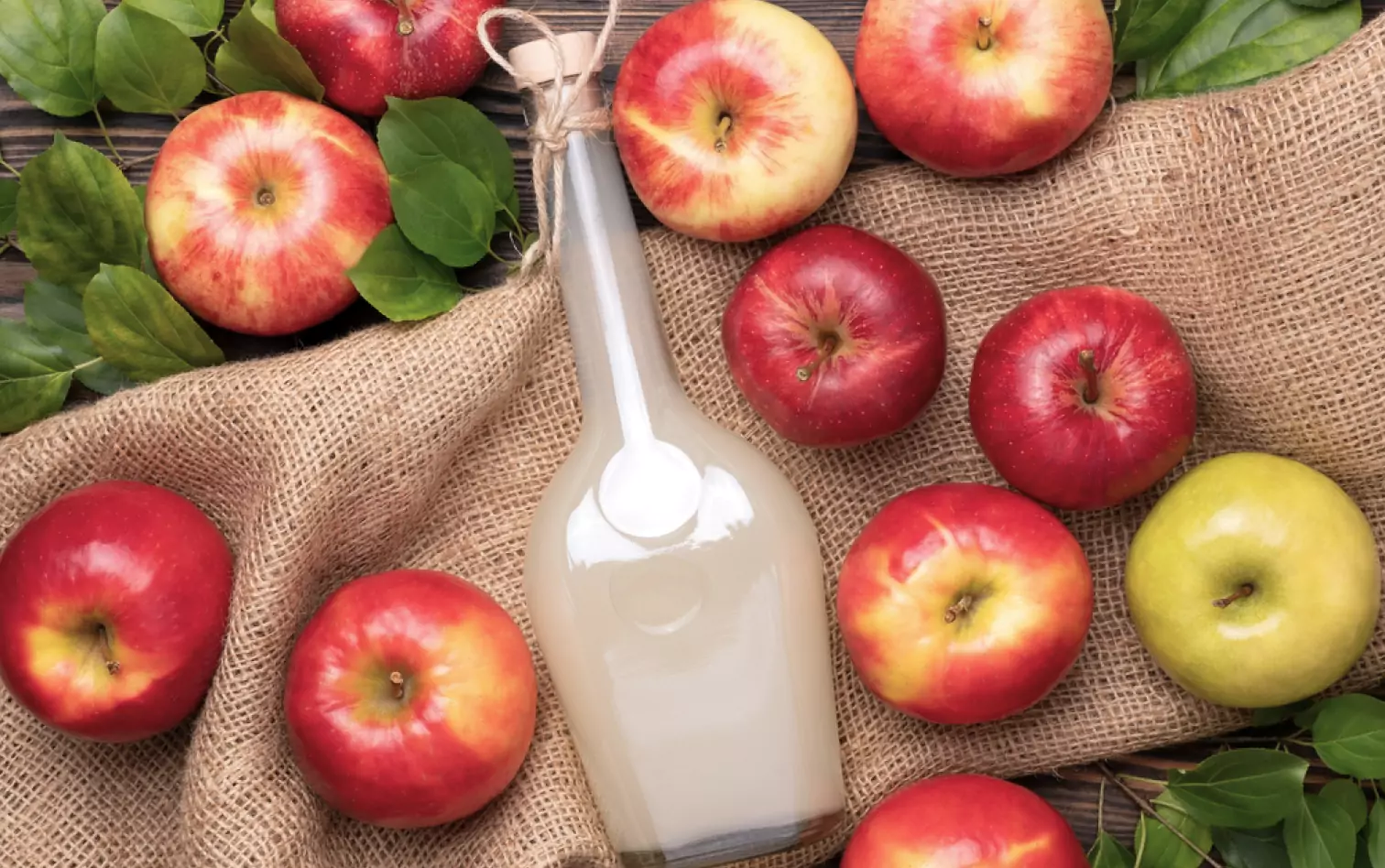 a bottle of vinegar and apples on fabric 