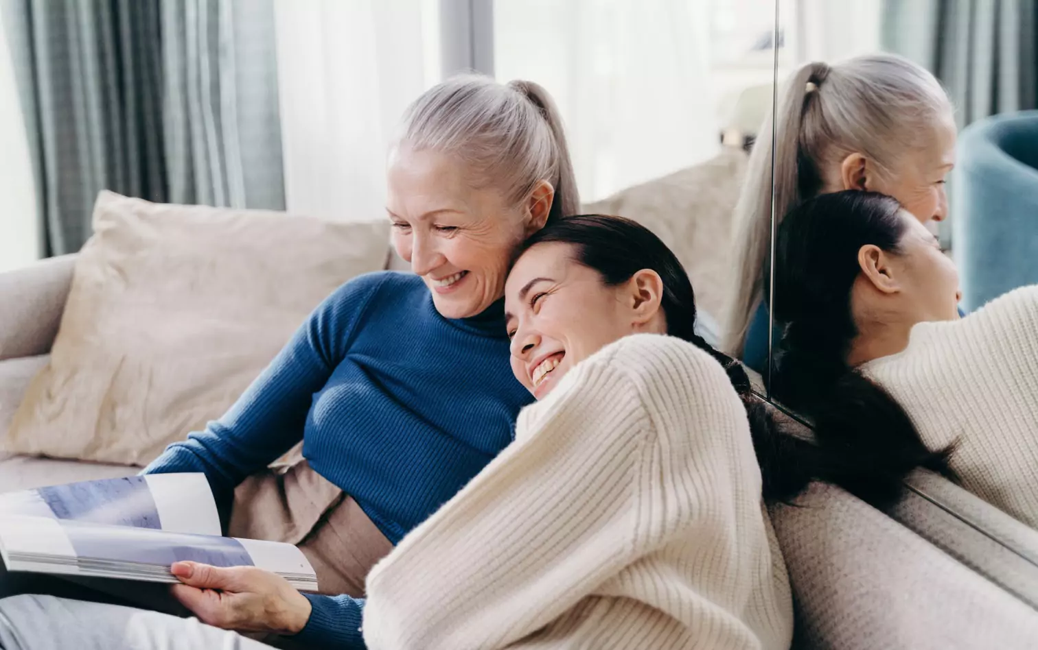 A mother and daughter on the couch together, laughing and reading a magtazine