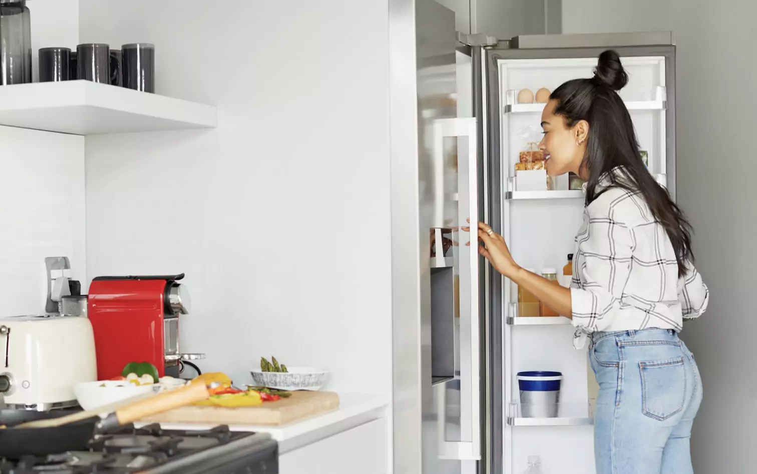 A woman in jeans and a shirt with long black hair looking in a fridge