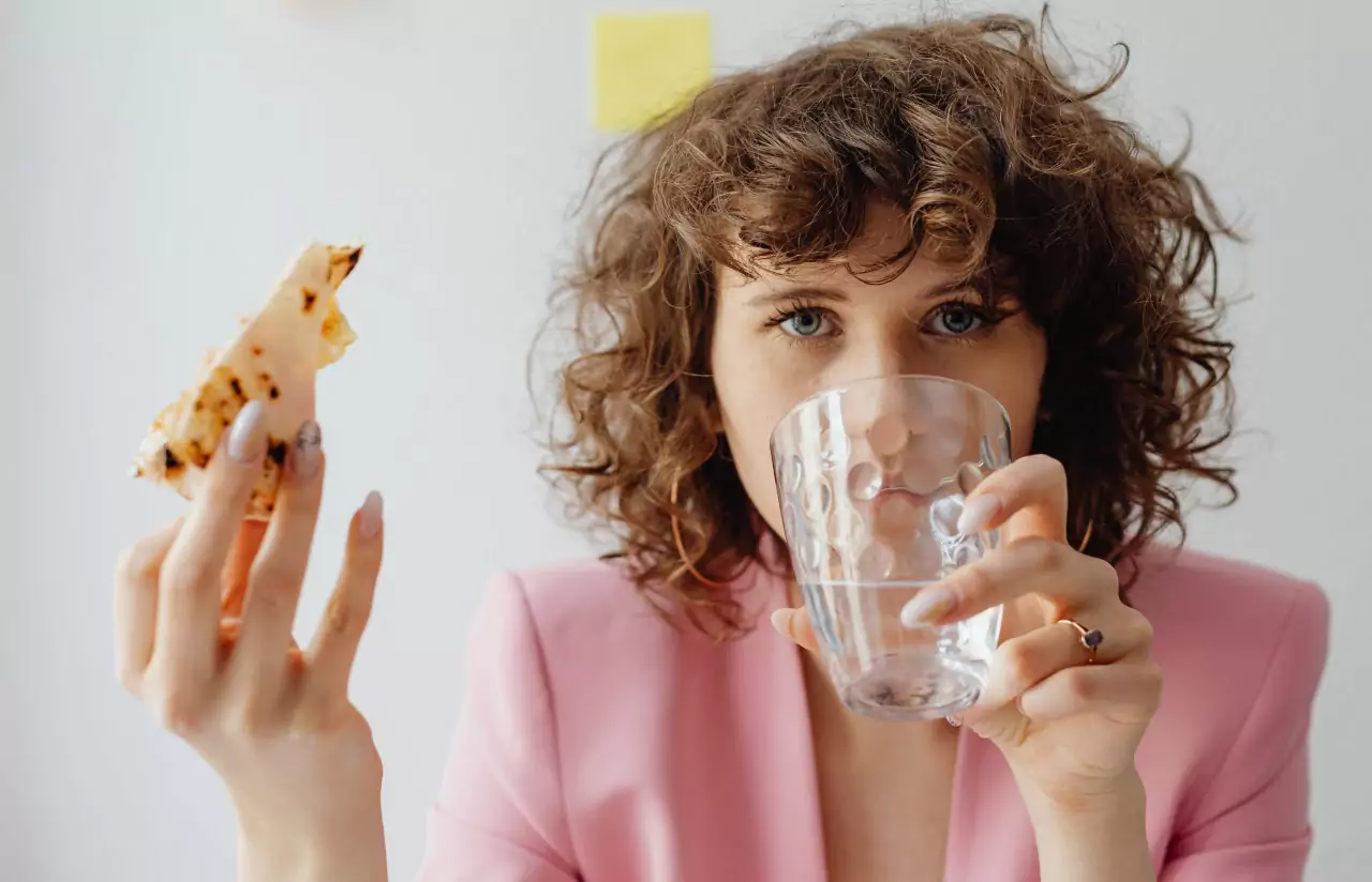 A person drinking water, holding a slice of pizza