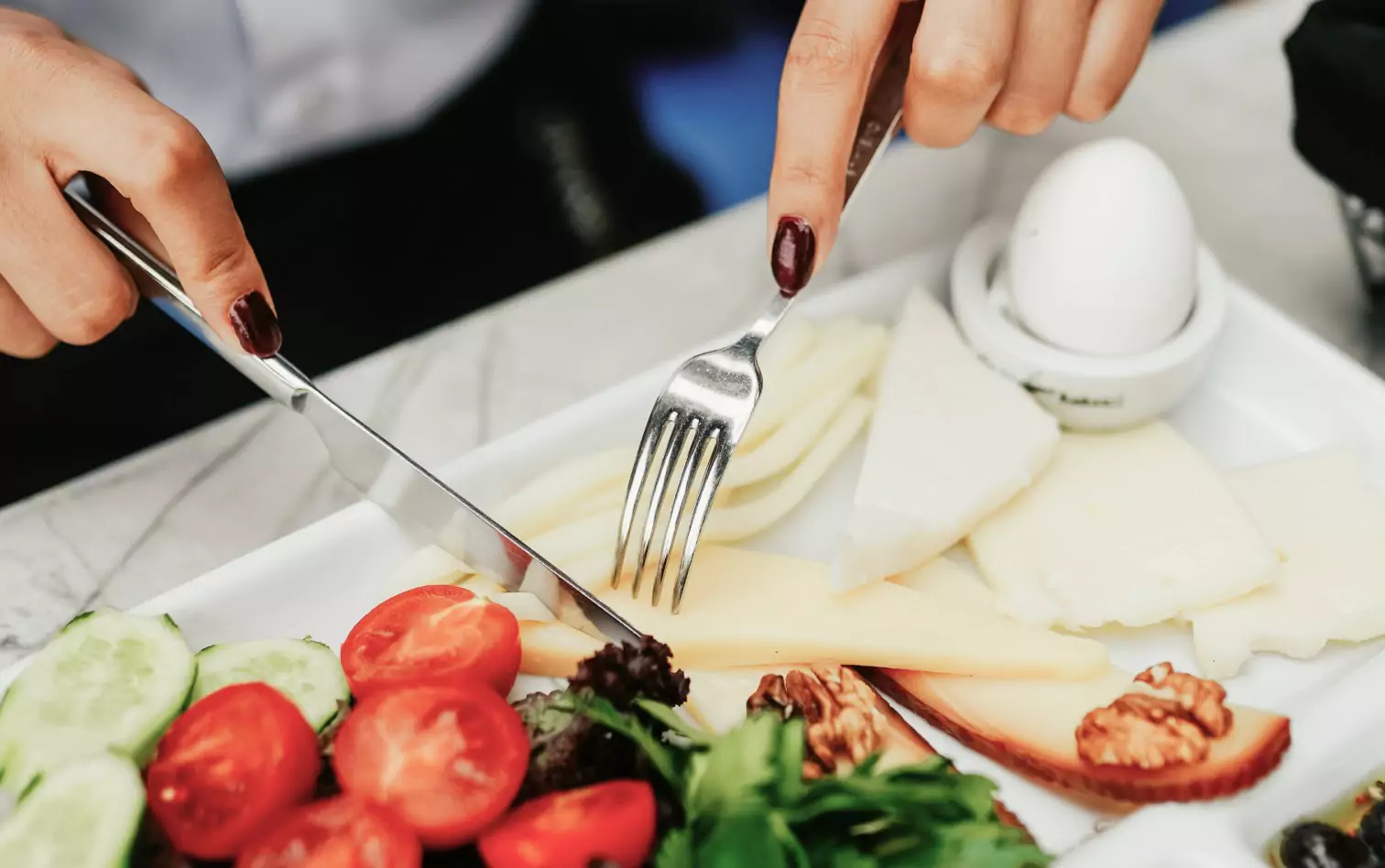 A person holding silverware over a plate of salad and cheese