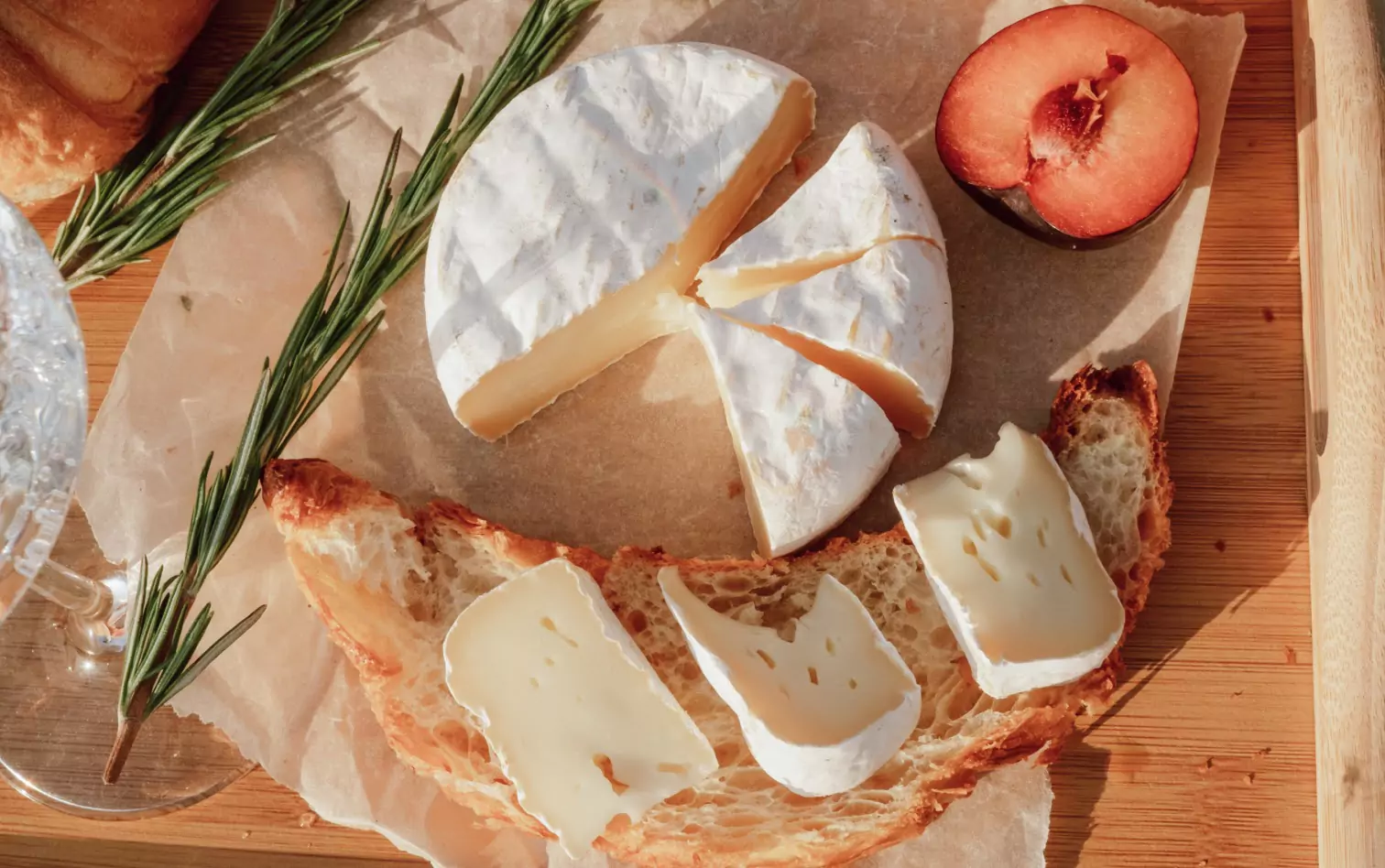 Brie cheese on a wooden board with rosemary fruits and bread