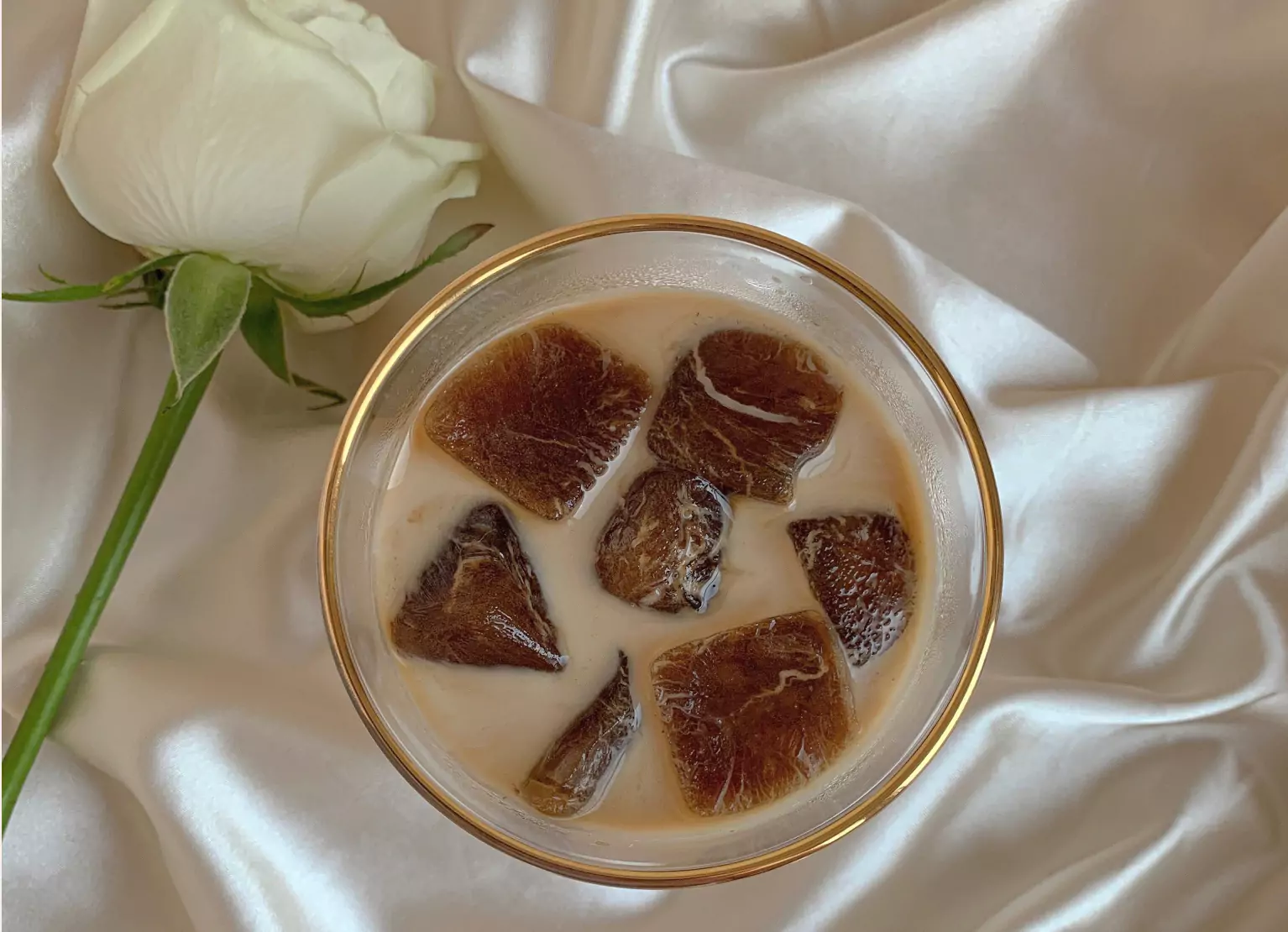 Iced coffee on silk sheet with white rose 