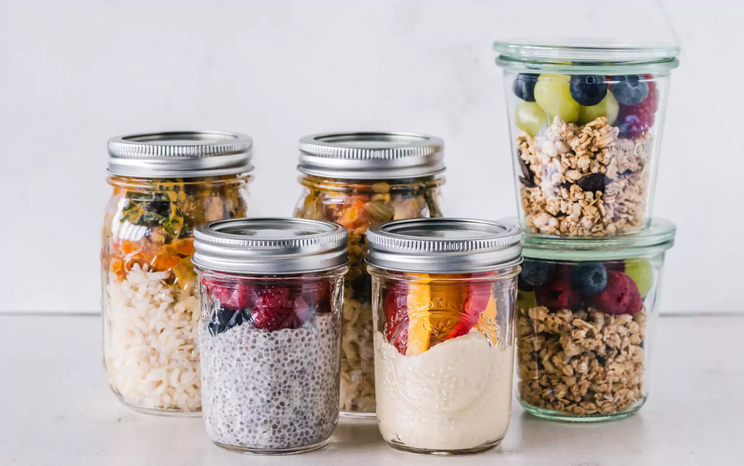 jars with different types of meals, granola with berries, rice with veggies and chia seeds pudding with berries