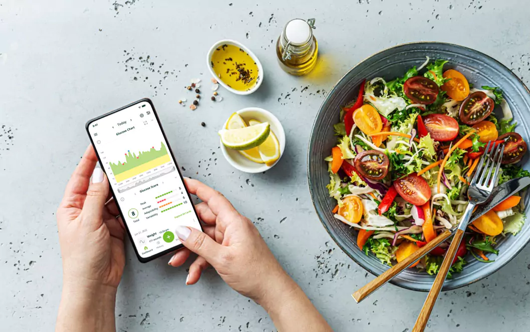 a person  checking glucose response on the Nutrisense app and a bowl of salad