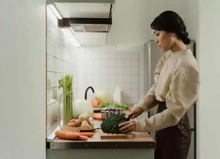 a person cutting broccoli on chopping board in kitchen