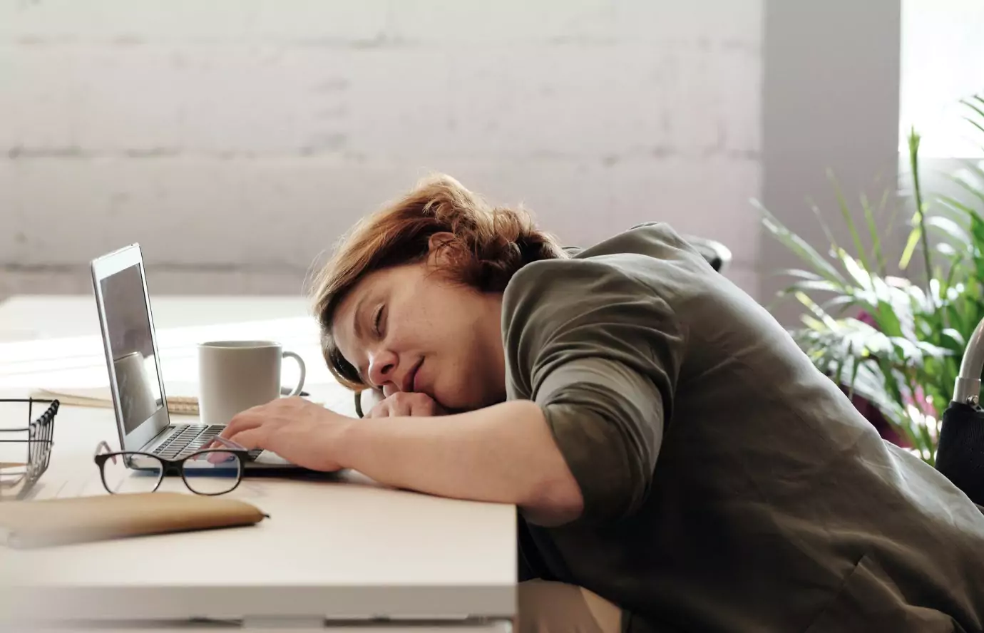 a person sleeping sitting at the table in front of a laptop 