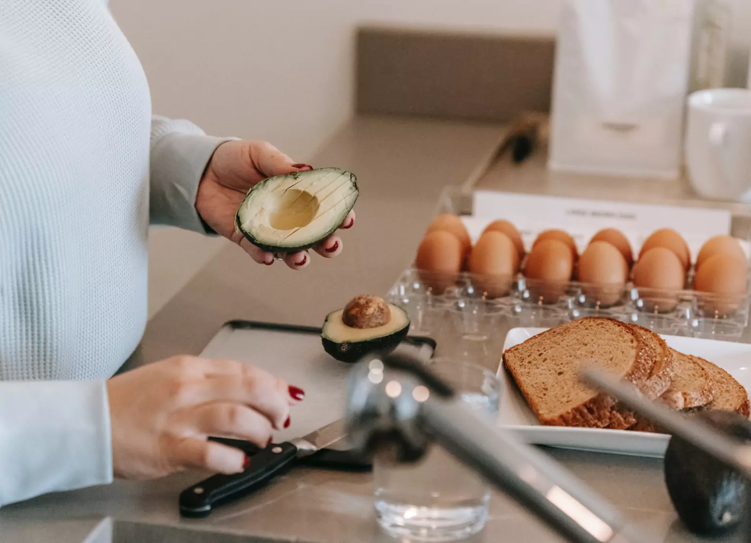 Woman making breakfast in kitchen with eggs, avocado, and toast