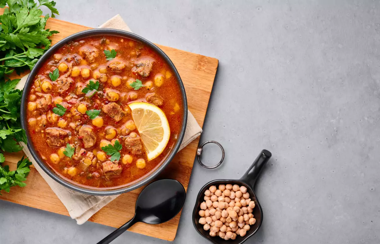 A bowl of bean stew on a wooden chopping board with cilantro alongside