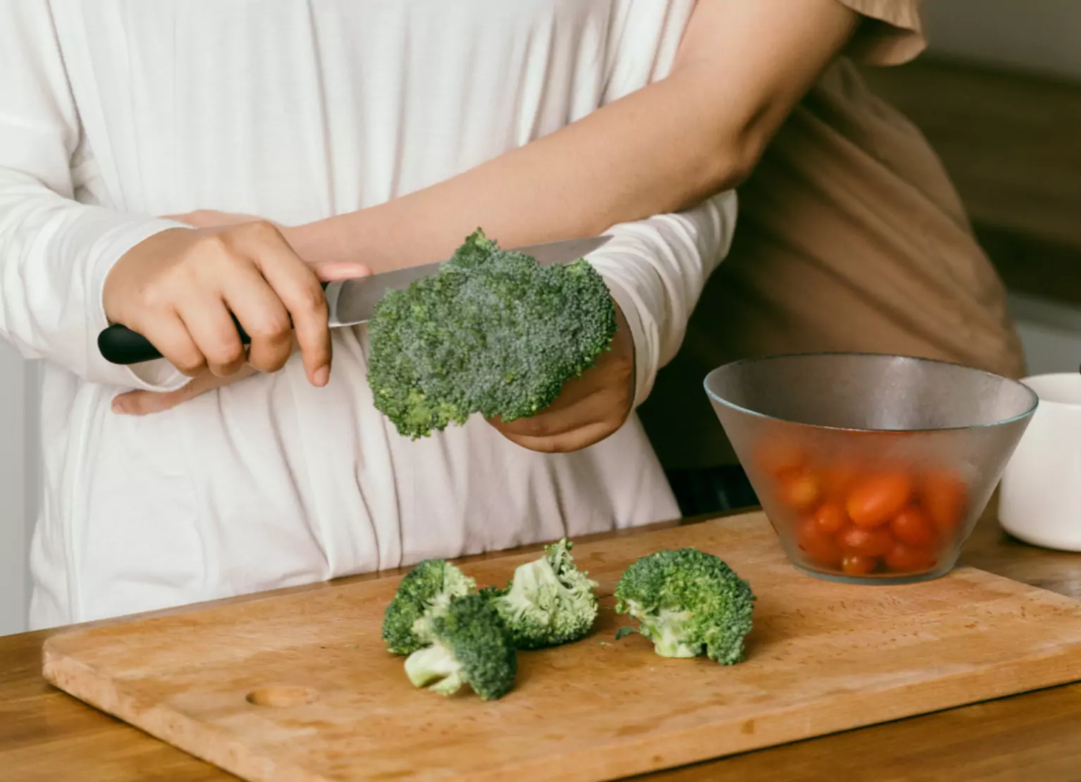 Person chopping broccoli on cutting board in kitchen