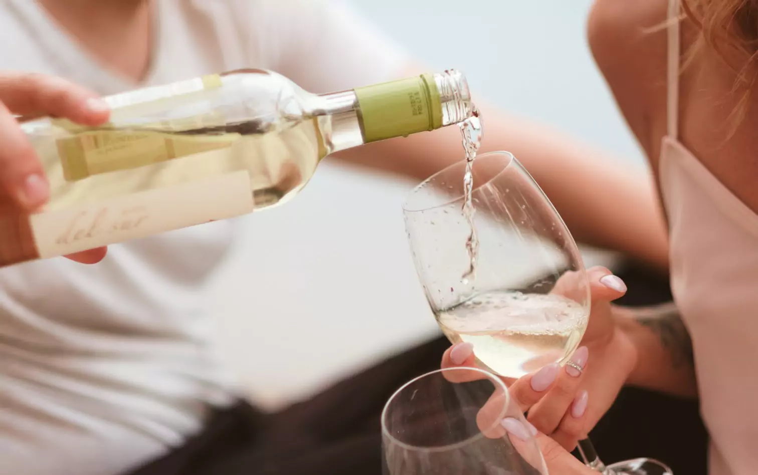 one person pouring white wine into a glass held by the other person