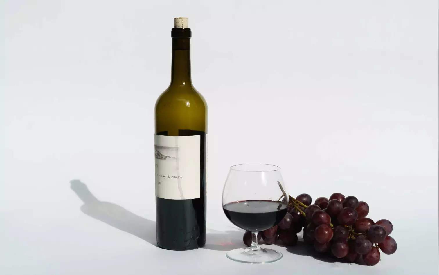 A bottle and glass of red wine alongside red grapes