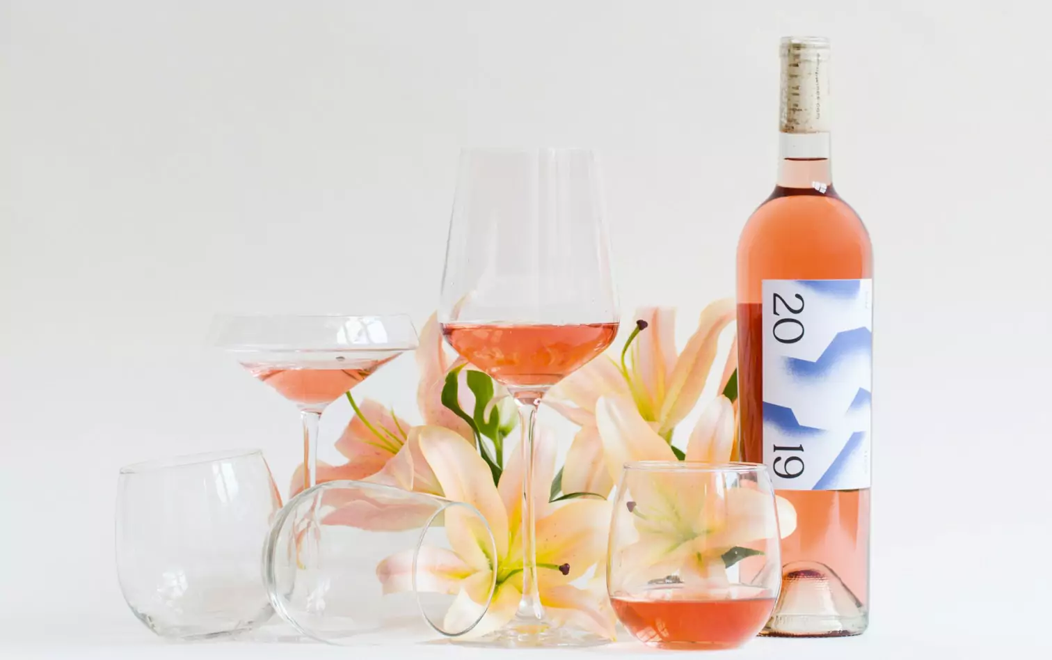 Glasses and a bottle of rose with flowers in the background