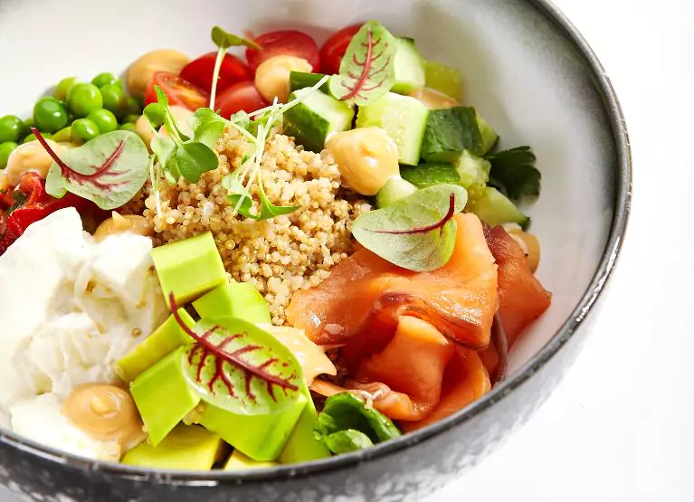 Couscous bowl with leafy greens, edamame, cucumbers, yogurt, tomatoes, avocado, and smoked salmon