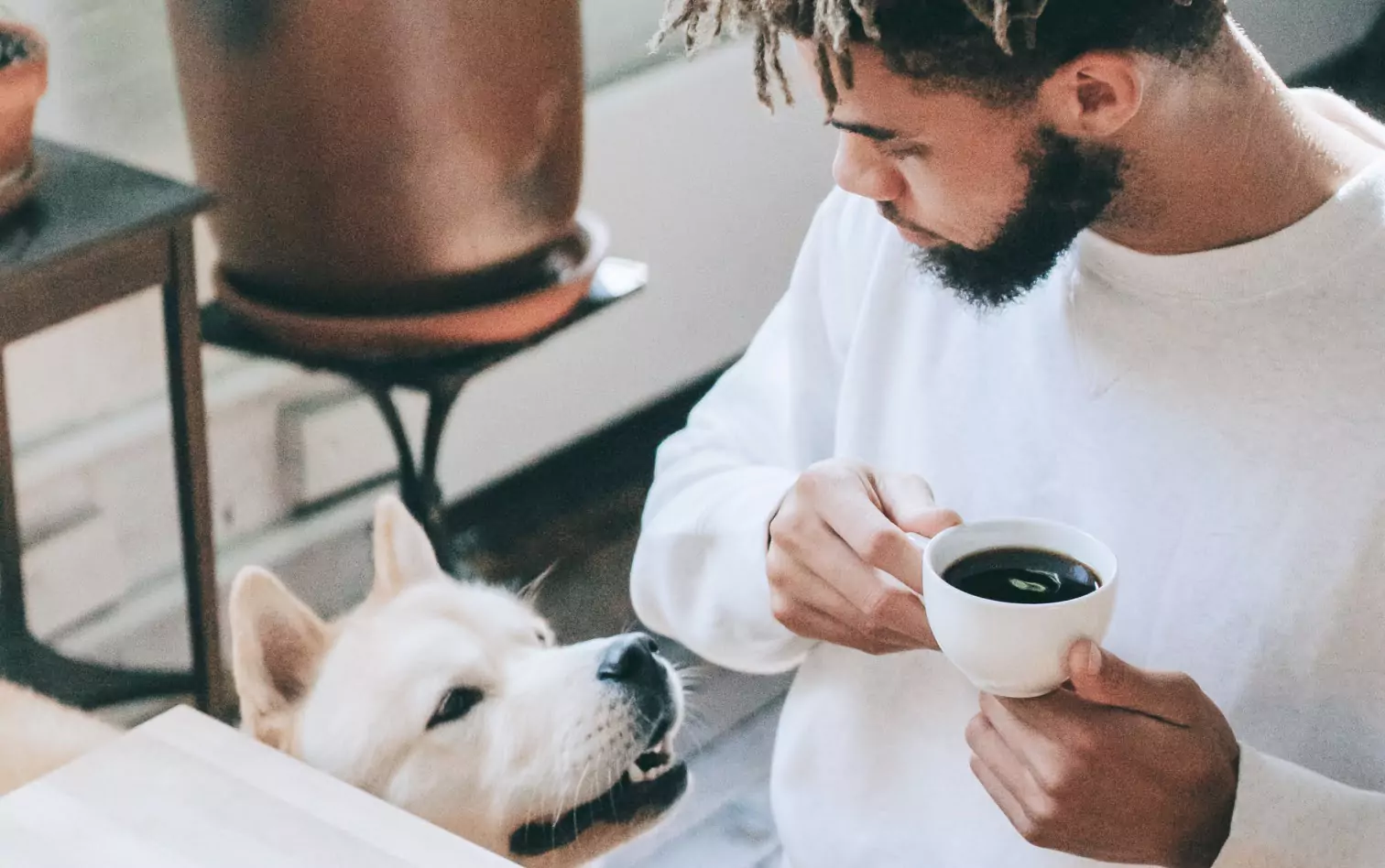 A man holding a cup of coffee looking down at a dog