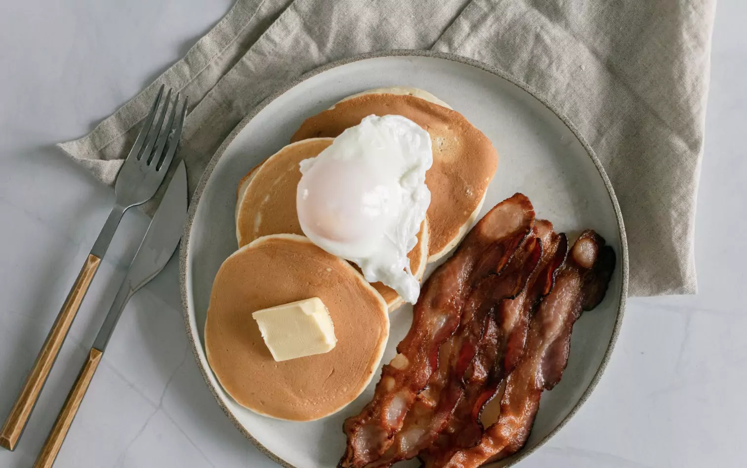 A p late of pancakes, a poached egg, a dot of butter and fried bacon