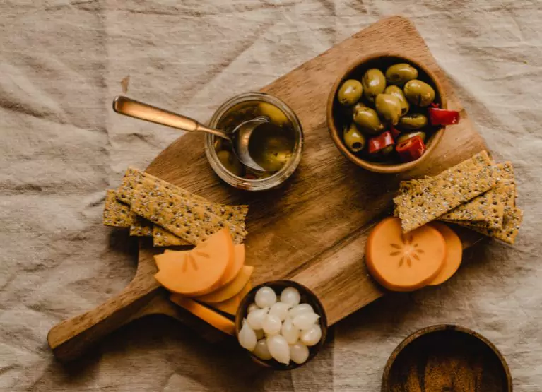 A board of olives, olive oil, crackers, and fruit