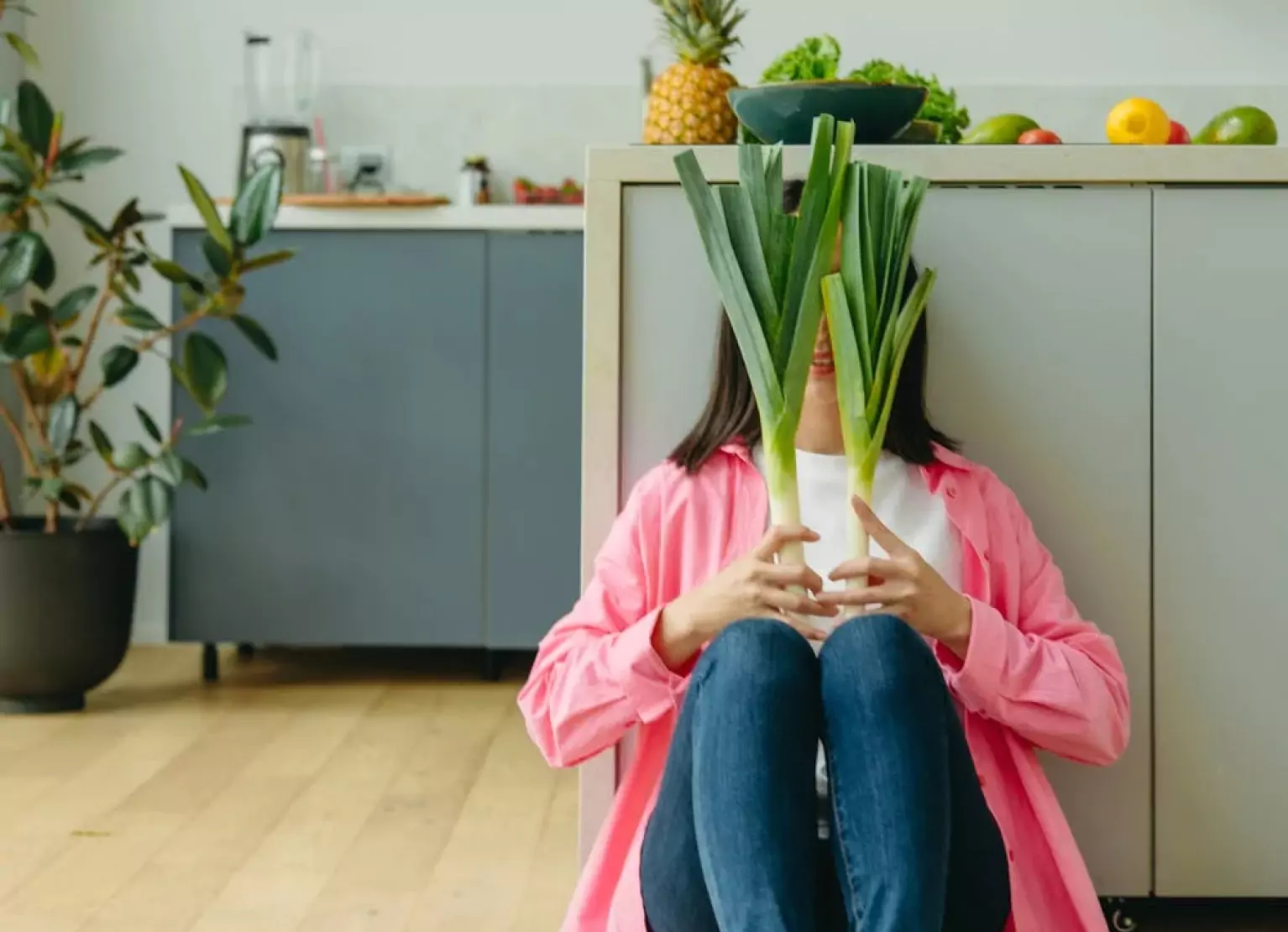 Person holding up green leafy veggies while sitting on the floor