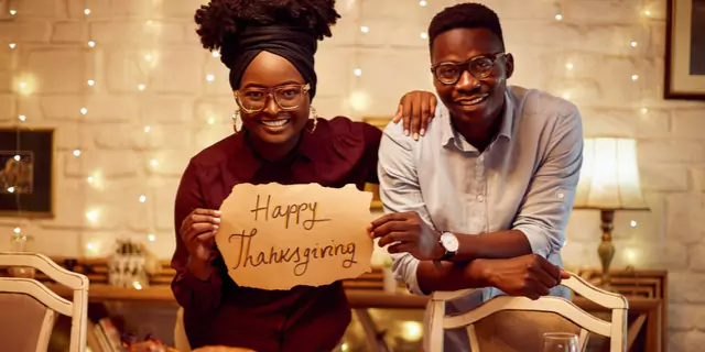 two people holding a piece of paper with words "Happy Thanksgiving" 