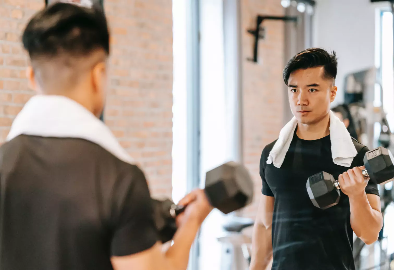 a person holding dumbbells in front of the mirror in the gym