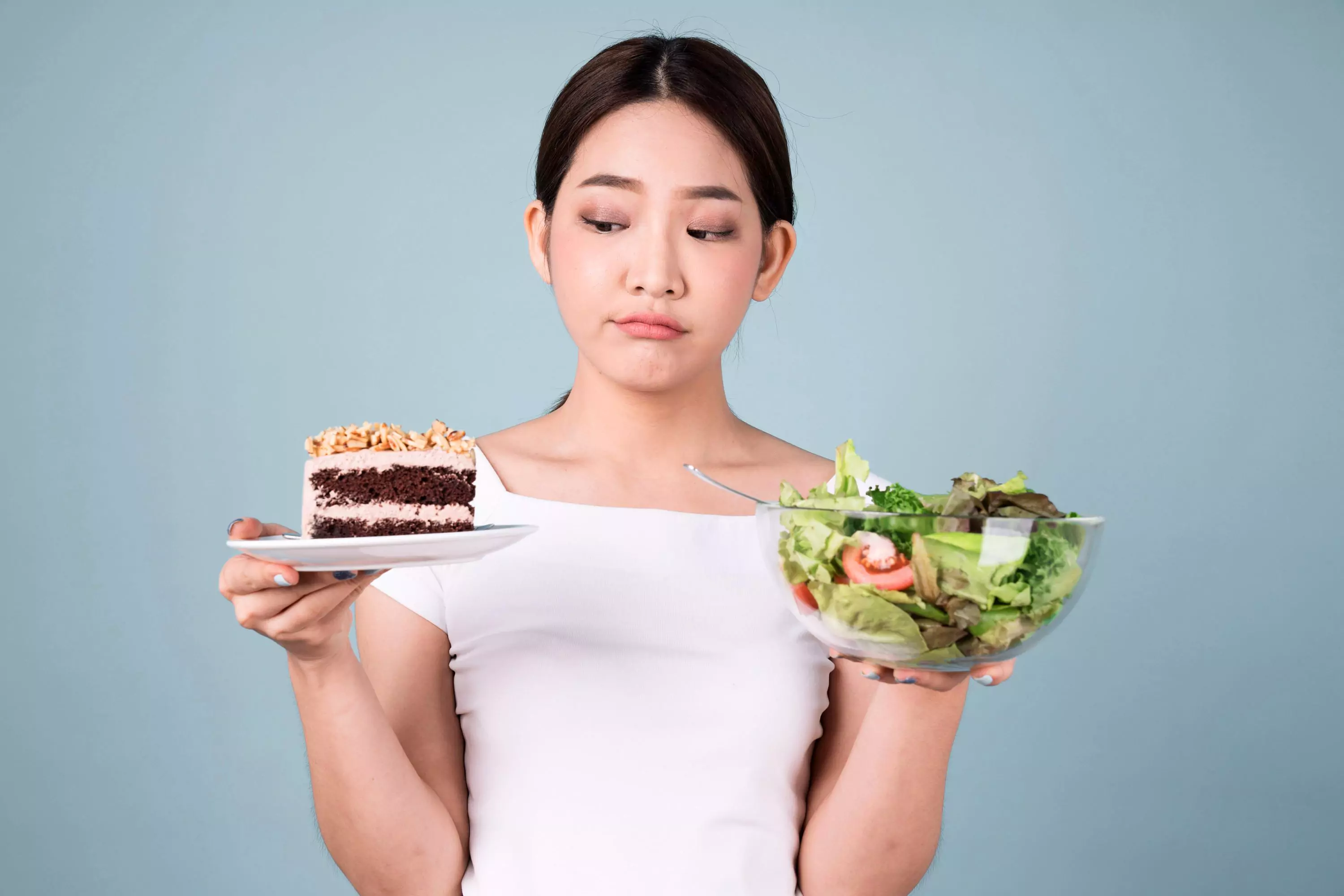 a person holding a plate of cake with one hand, and a bowl of a salad with another