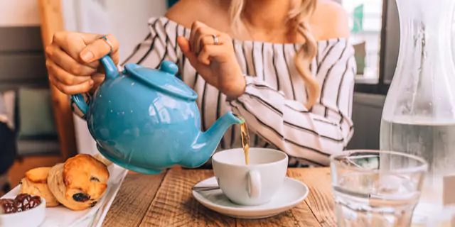 a person pouring tea from a teapot in a cup