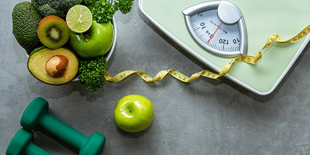 a scale, a tape measure, dumbbells and a bowl of veggies and fruits