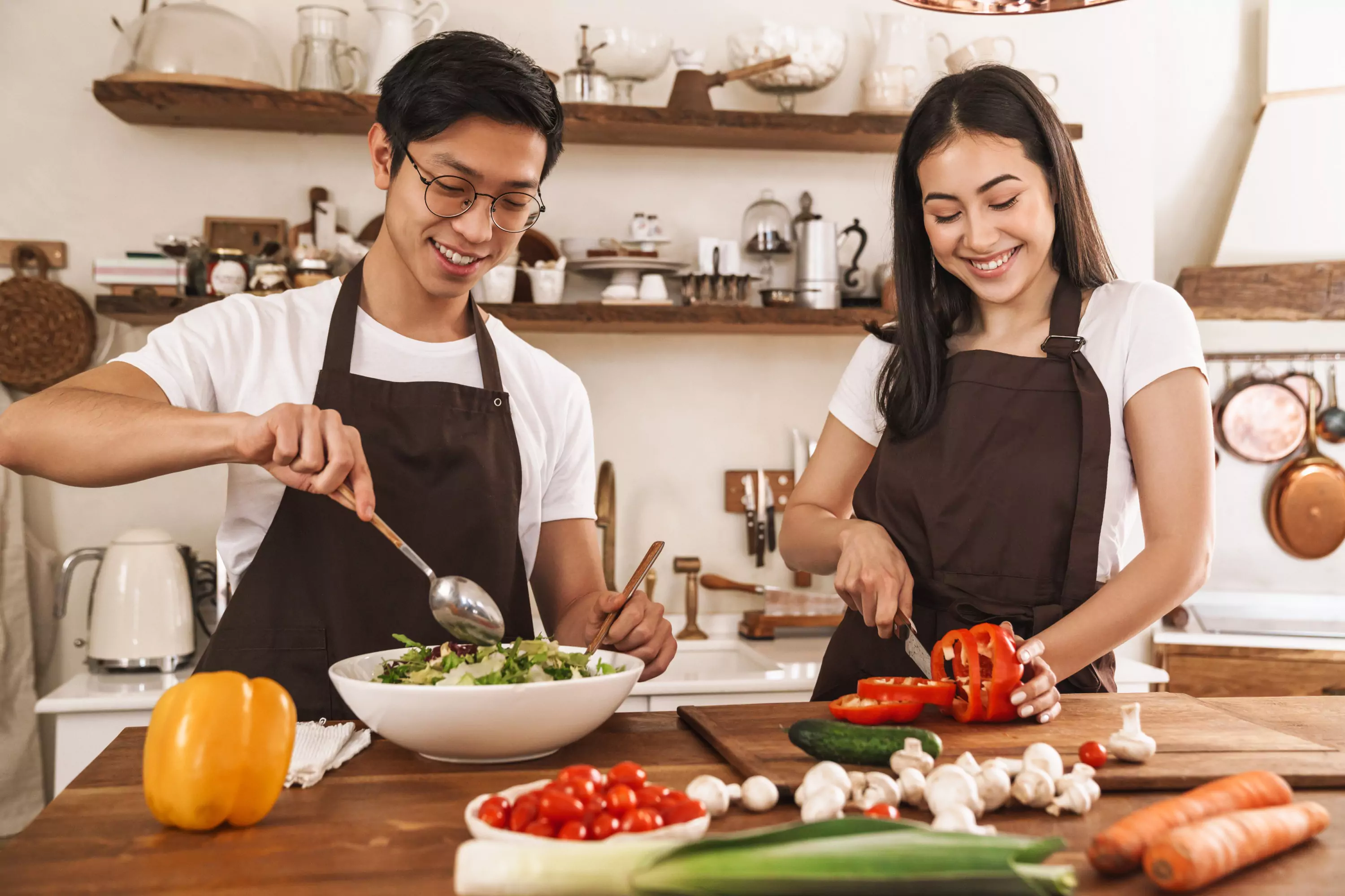 a couple of people making a salad in the kitchen 