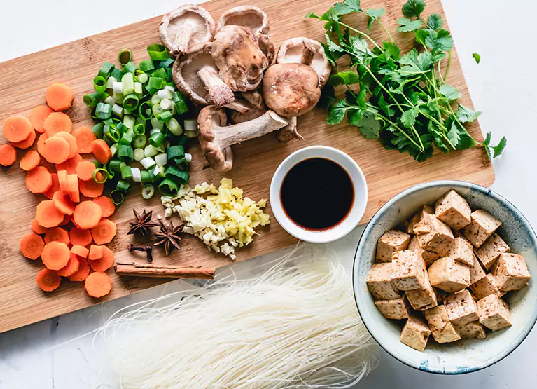 Cutting board with chopped up green onions, carrots, cilantro, tofu, soy sauce