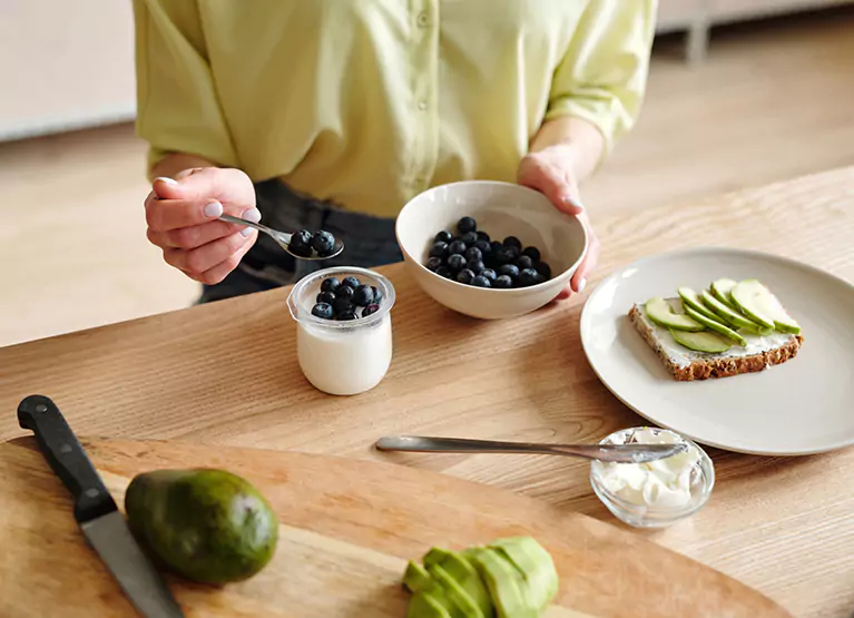 Person eating blueberries with yogurt and avocado toast