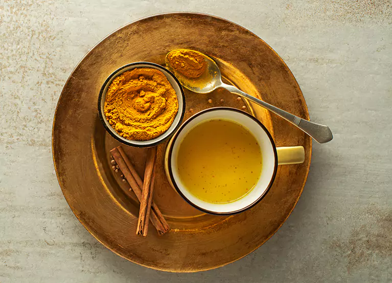 Tea cup holder holding golden milk latte and bowl of turmeric powder