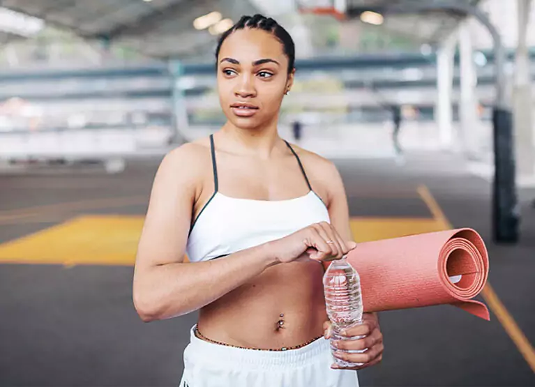 Woman holding pink yoga mat and plastic water bottle