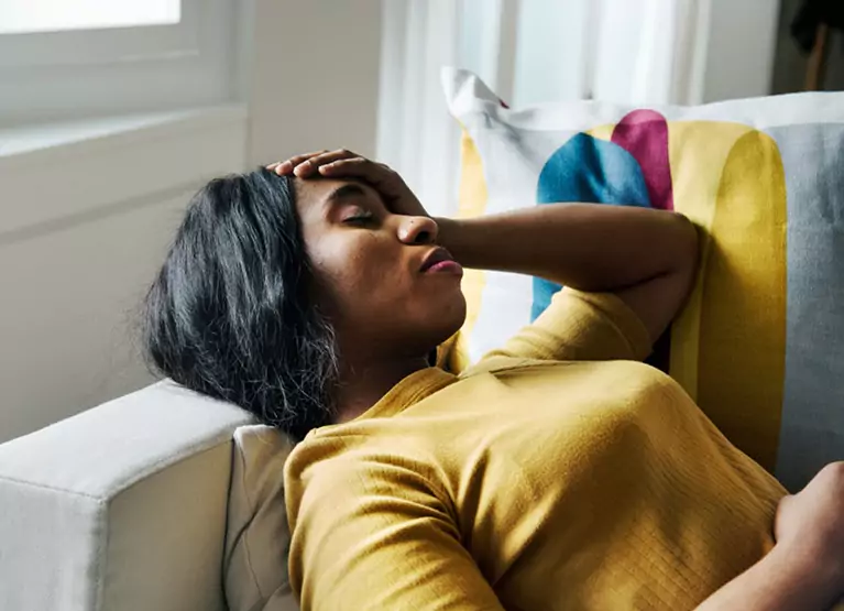 Woman laying on couch and touching her forehead