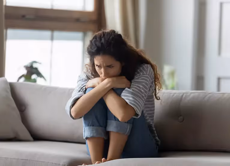 Frowning woman with knees curled up on the couch