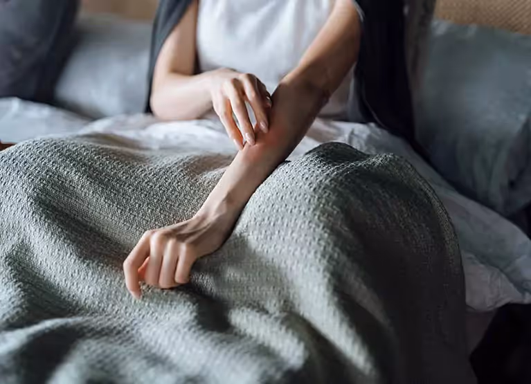 Person touching arm with hand while sitting in bed