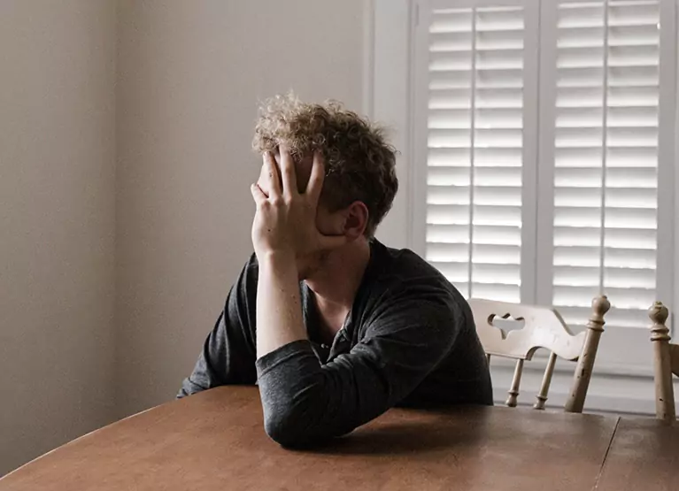 Distraught man sitting at dining table holding his head