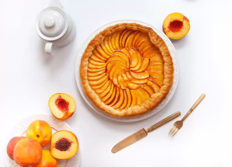 a peach tart on a table with cutlery and fresh peaches