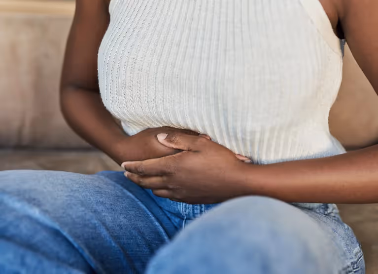 Torso of a woman in a white top and blue jeans, holding her stomach