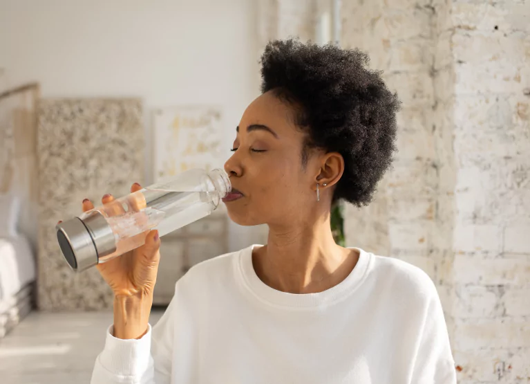 A woman in a white top drinking water from a bottle 