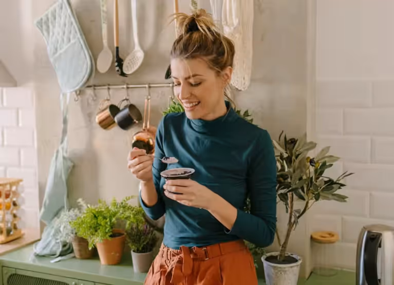 Woman with hair up in a kitchen eating yogurt