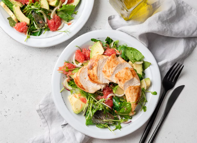 Two plates of leafy greens, avocado, grapefruit, and chicken breast